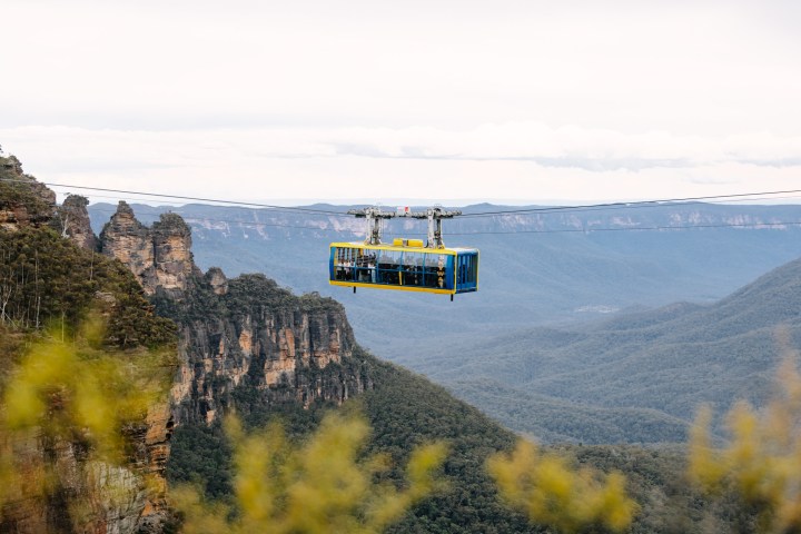 Cable car over forested valley with rock formations and mountains in the background.