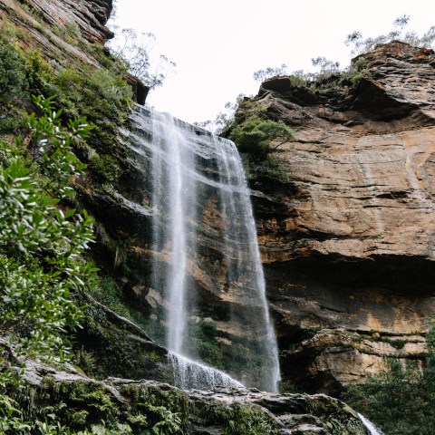 Waterfall cascading down a rocky cliff with surrounding greenery.