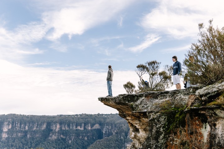 Two people stand on a rocky cliff edge overlooking a vast canyon.