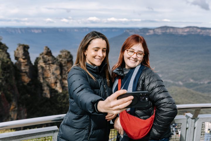 Two women taking a selfie with scenic mountain view in the background.