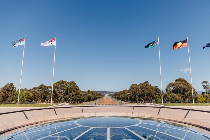 Flags on poles with clear sky and trees in the background, viewed from a building terrace.