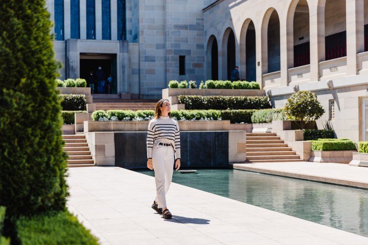 Person in striped sweater walking by a reflective pool in a formal garden setting.
