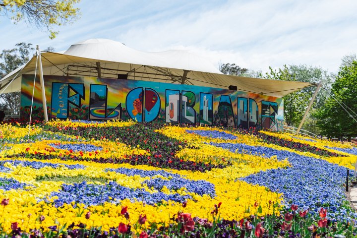 Colorful flower beds with a large sign reading 'FLORIADE' beneath a tent canopy.