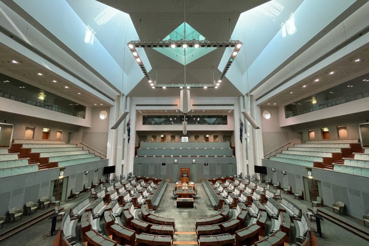 Spacious government chamber with rows of seats, central podium, and bright overhead lighting.