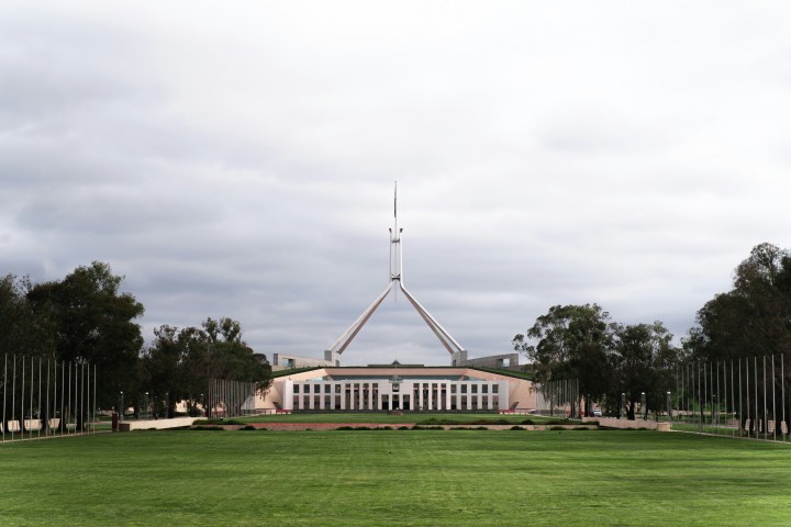 Building with large grass field and flagpole under cloudy sky.