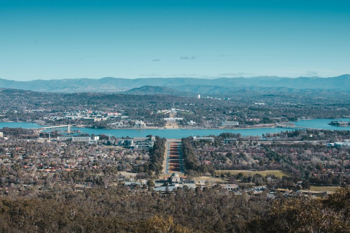 Aerial view of a city with a body of water and mountains in the background under a clear blue sky.