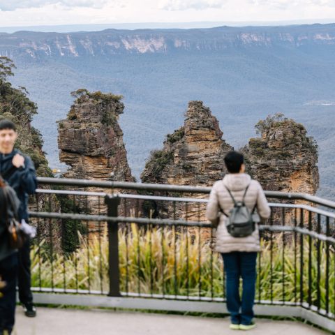 People at a railing overlook with the Three Sisters rock formation in the background.