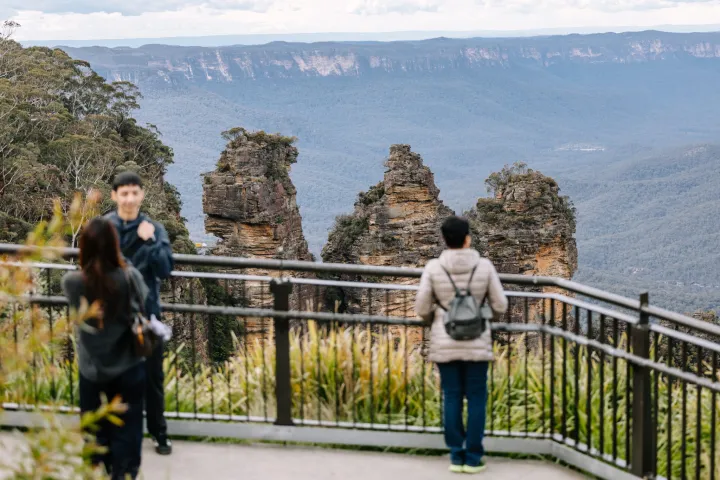 People at a railing overlook with the Three Sisters rock formation in the background.