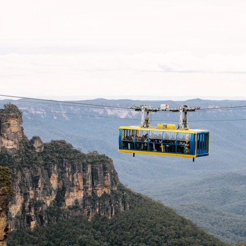 Aerial cable car with passengers traveling over forested mountains.