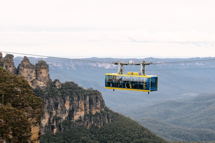 Aerial cable car with passengers traveling over forested mountains.