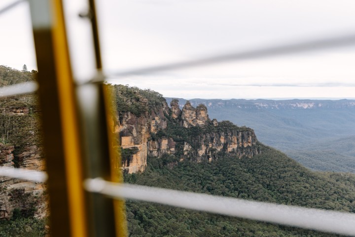 View of mountain cliffs through a cable car window with trees below.