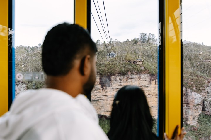 Two people viewing a cable car and cliffside through yellow-framed windows.