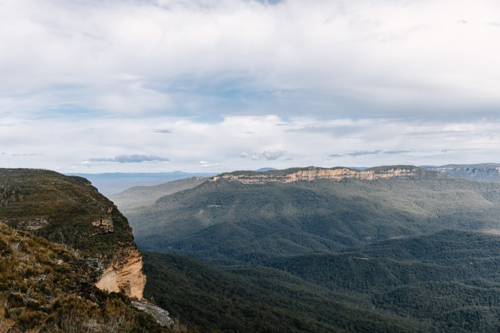 Scenic view of forested mountains and cliffs under a cloudy sky.