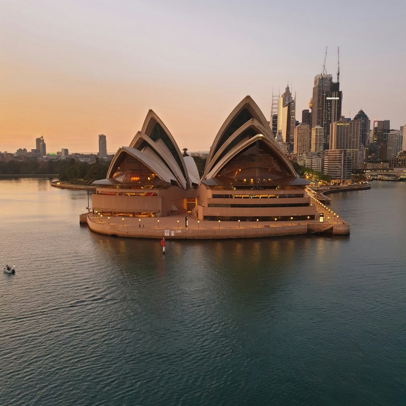 a small boat in a large body of water with Sydney Opera House in the background