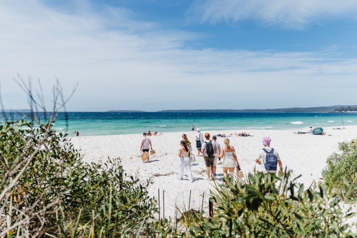 Group of people walking towards a sunny beach with white sand and turquoise water.