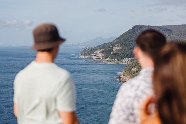 Three people look at a coastal landscape with cliffs and ocean.