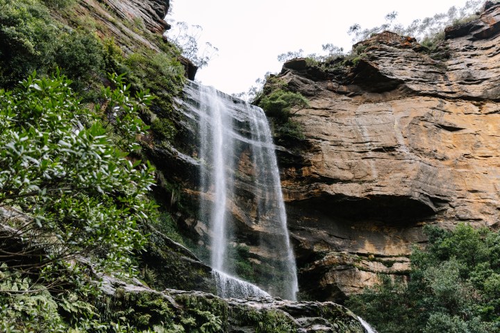 Waterfall cascading down rocky cliffs with lush greenery.