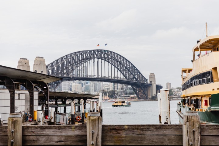 Sydney Harbour Bridge view with ferries in the foreground on a cloudy day.