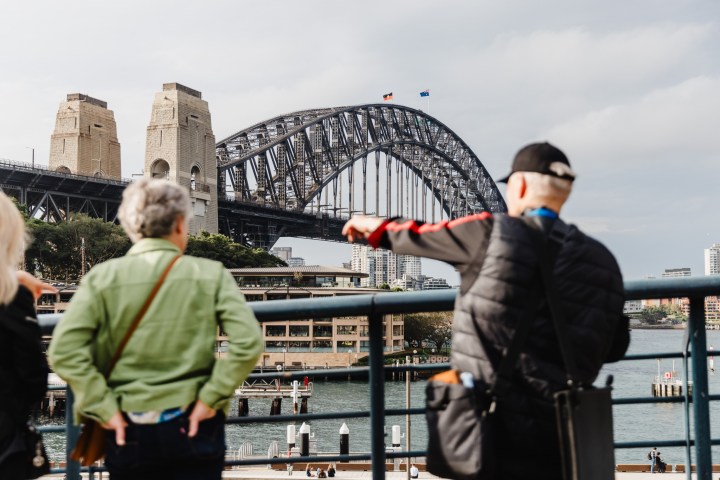 Two people admire the Sydney Harbour Bridge from a waterfront viewpoint.