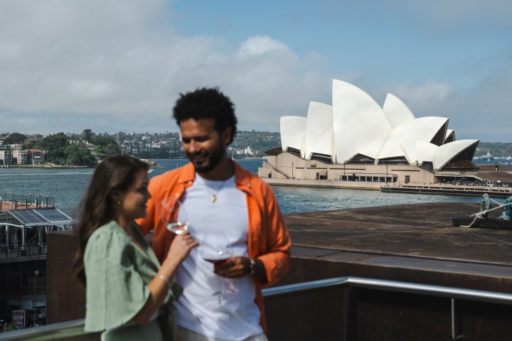 Two people in front of Sydney Opera House with drinks.