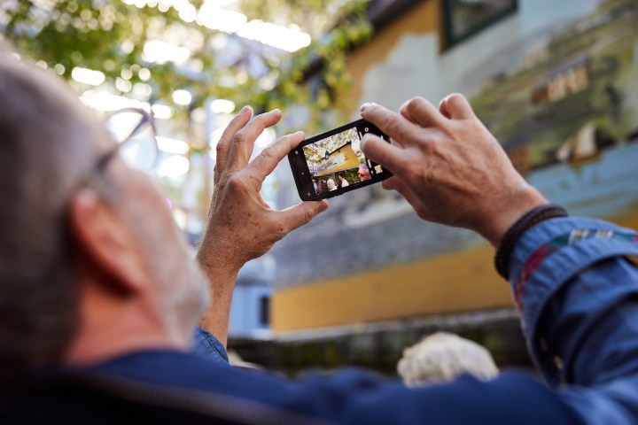Person taking a photo of wall mural with smartphone outdoors.