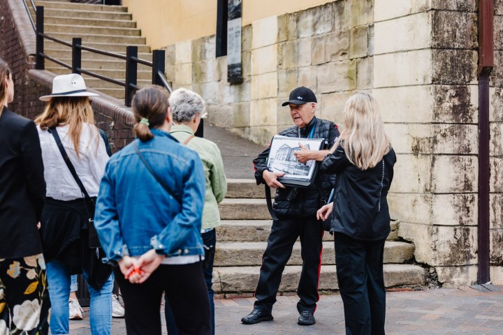 Guide holding images speaks to a tour group by stone steps.