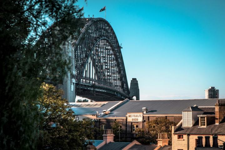 View of Sydney Harbour Bridge over rooftops and trees under a clear blue sky.