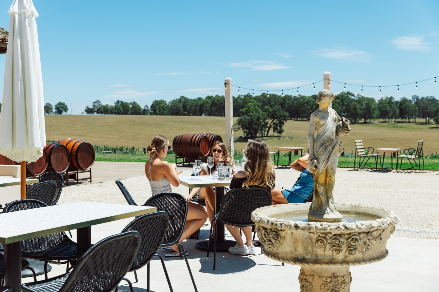 People sit at outdoor tables near a fountain in a winery setting.