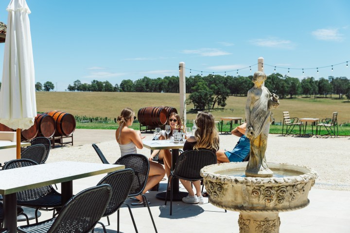 People sit at outdoor tables near a fountain in a winery setting.