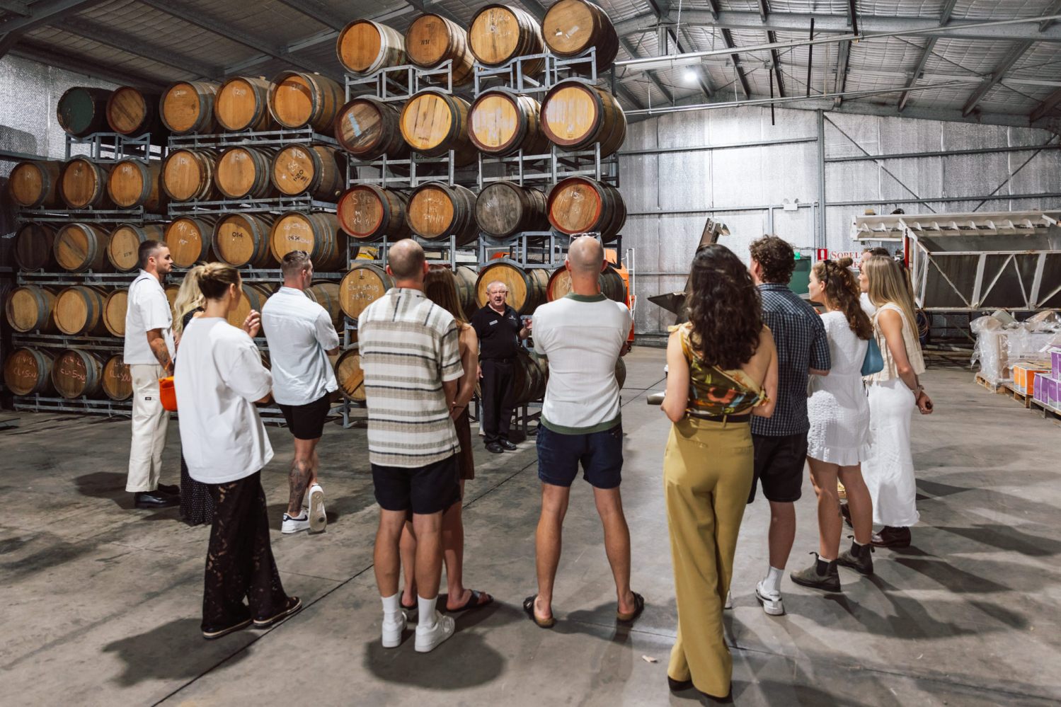 Group of people in winery cellar with wine barrels.