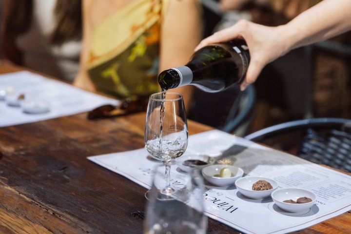 Wine being poured into a glass on a wooden table with small dishes of food.