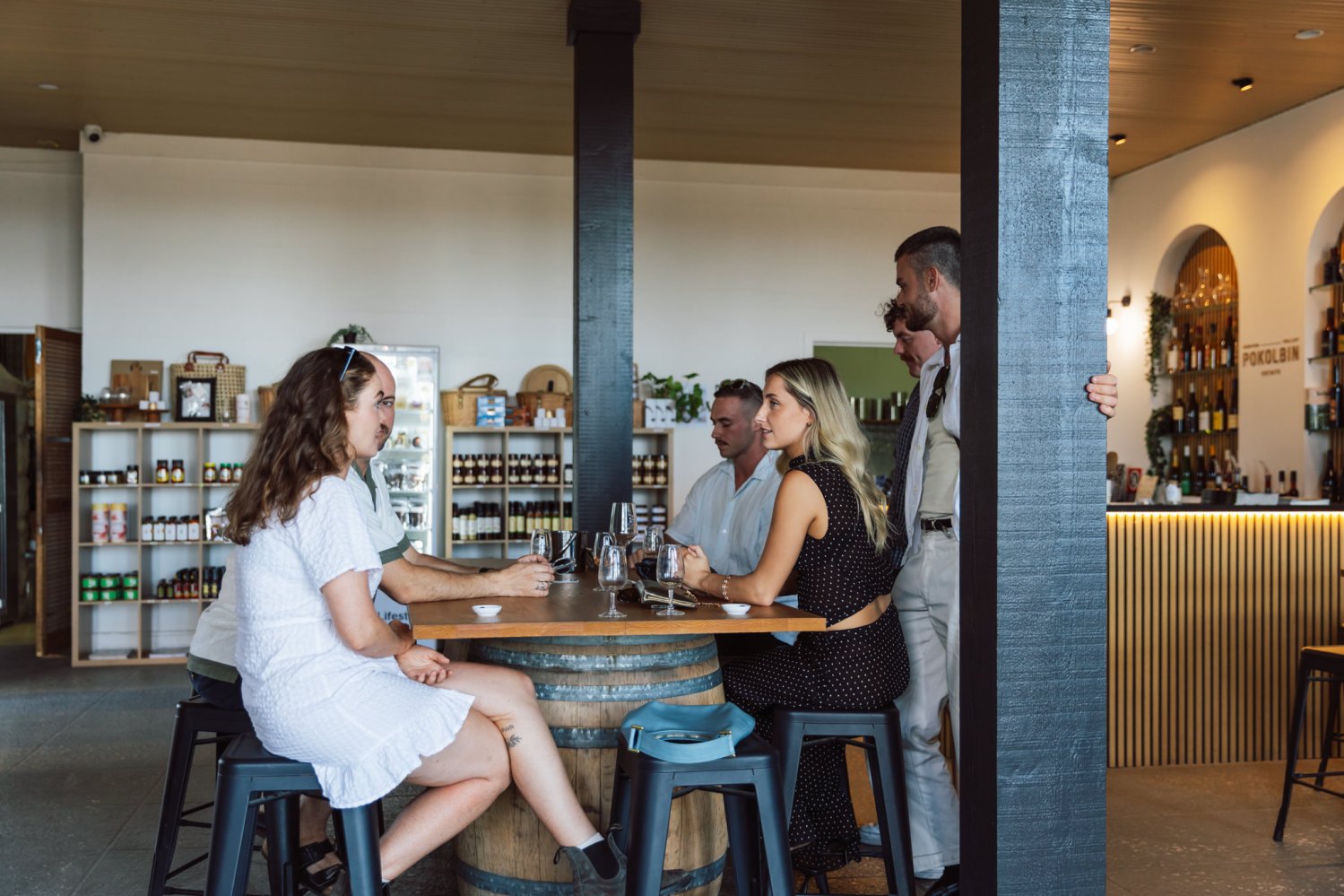 Five people chatting around a wine barrel table in a modern tasting room.