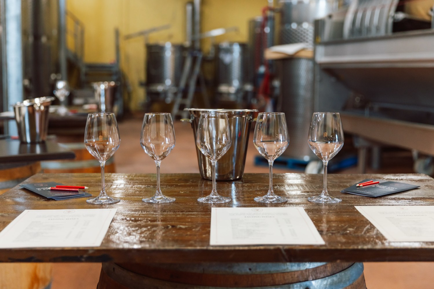 Five empty wine glasses on a table in a winery setting.