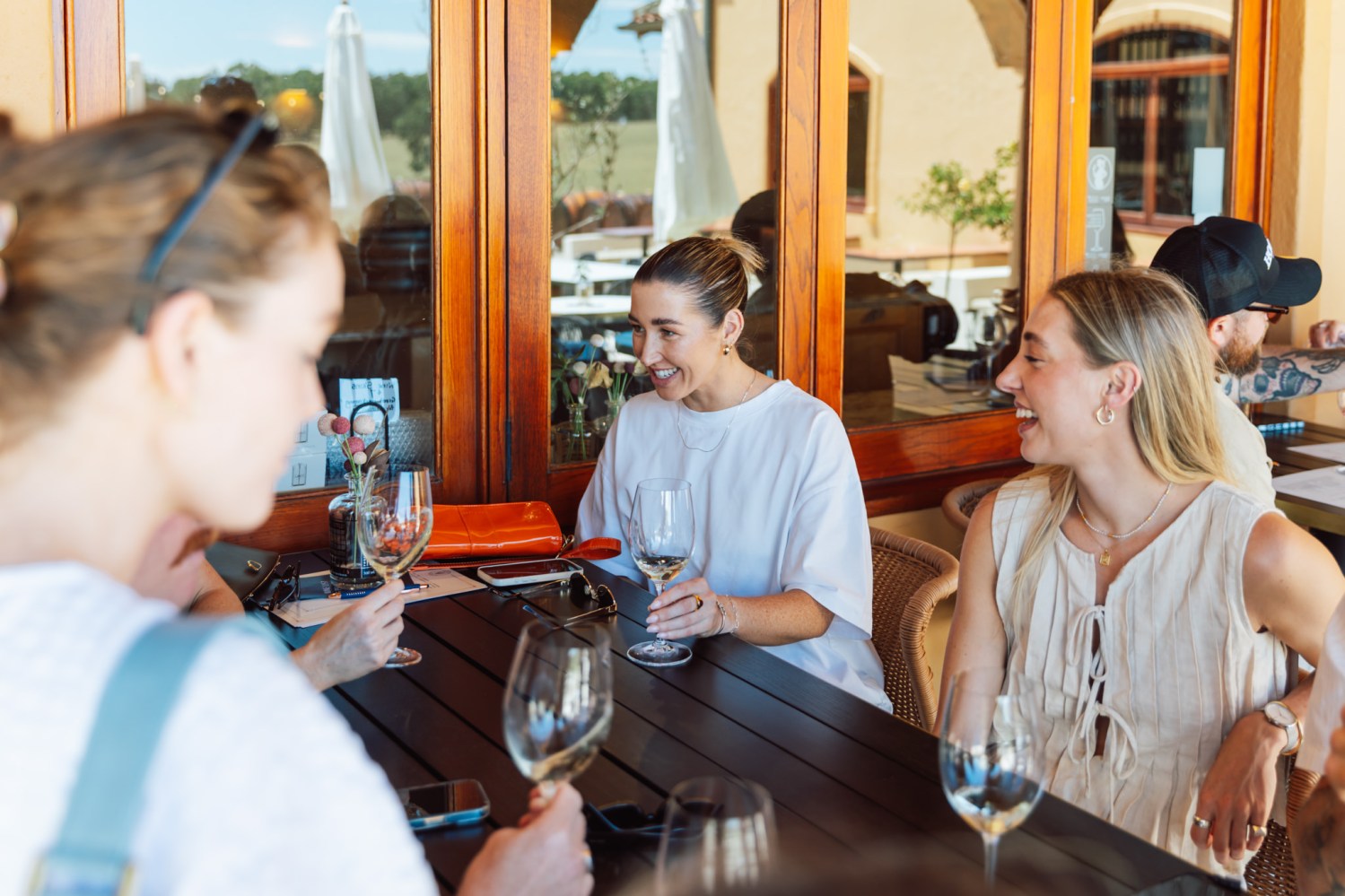 Four people sitting outside at a table, holding wine glasses, and smiling.