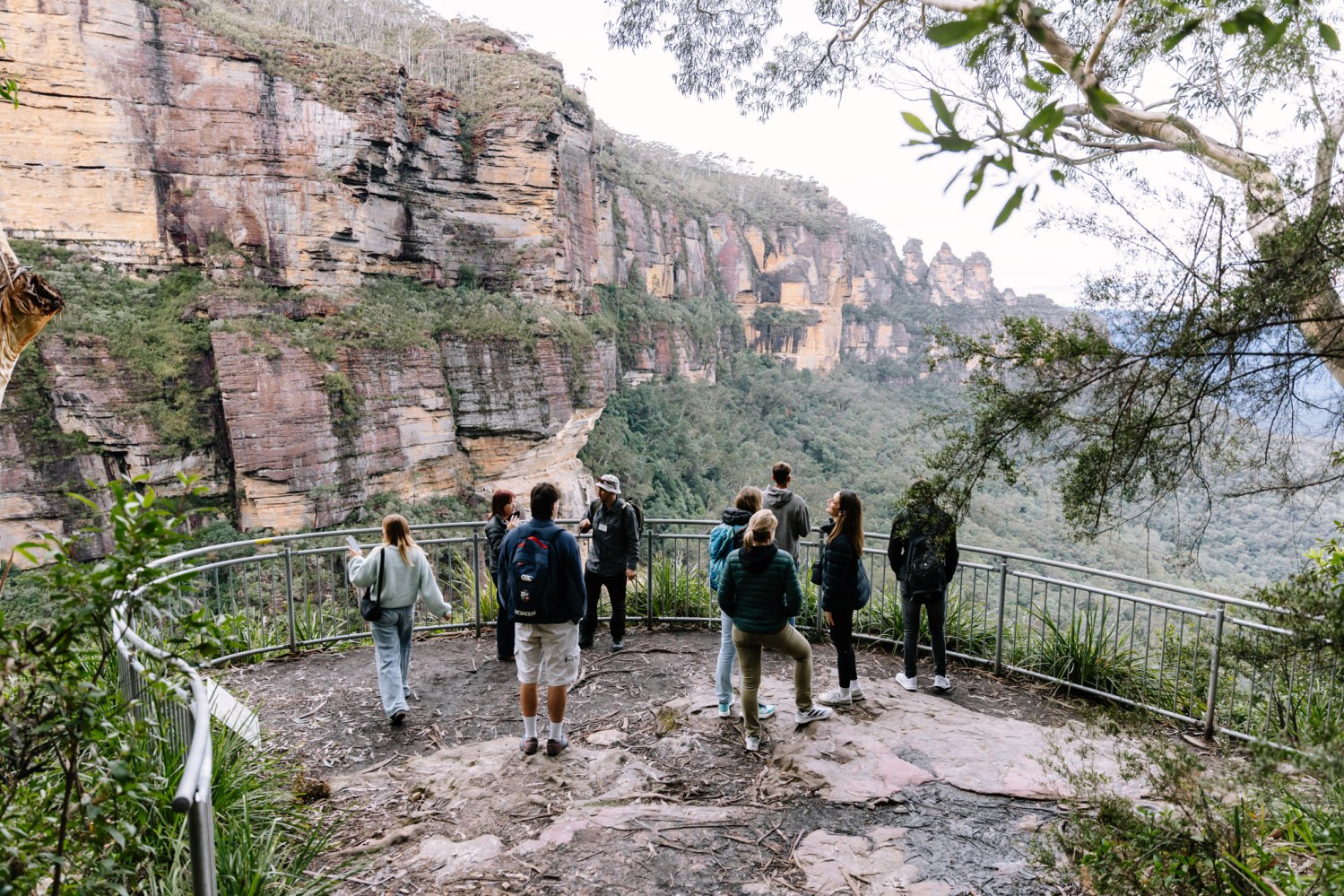 Group of people at a mountain viewpoint with railing and rocky cliffs.