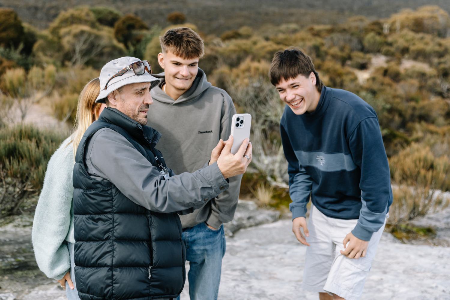 Four people outdoors looking at a phone and smiling.