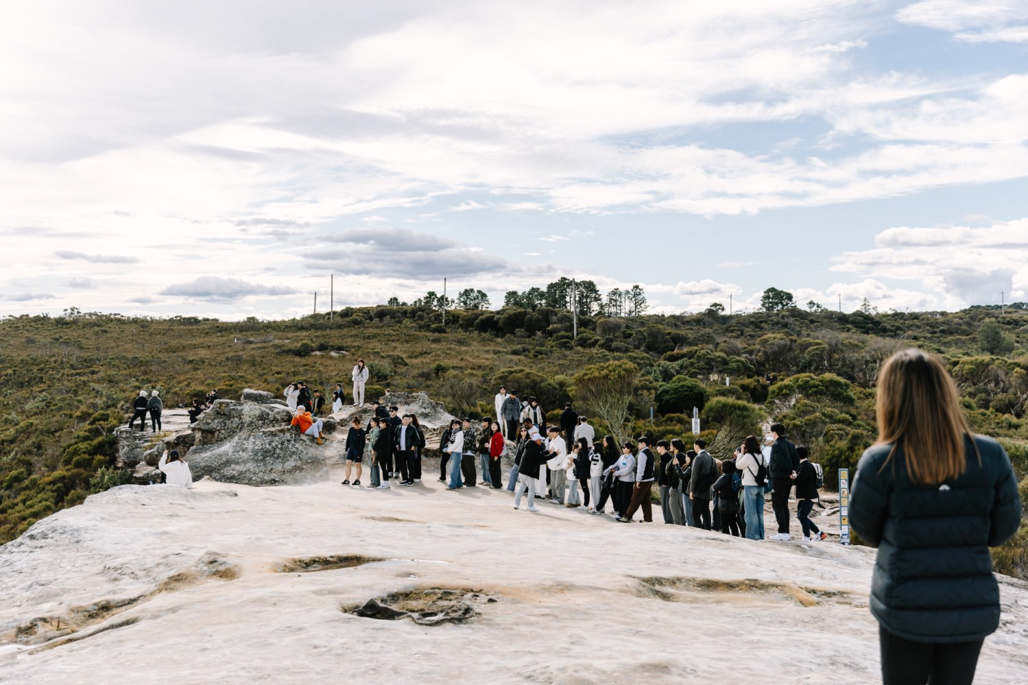 Group of people walking on a rocky landscape under a cloudy sky.